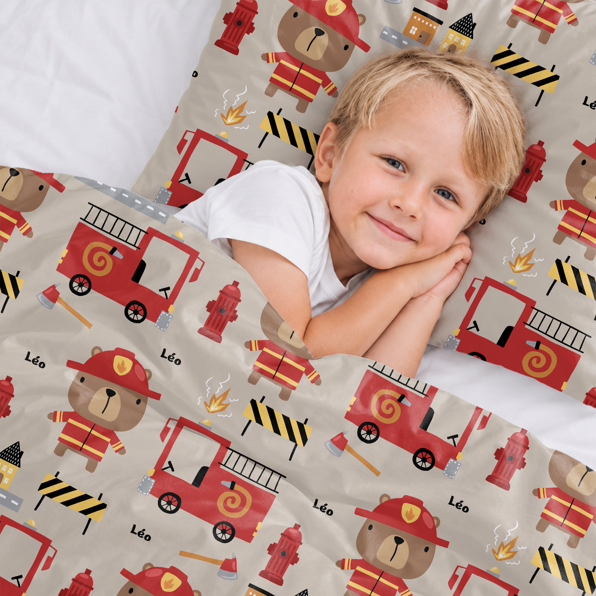 Petit garçon blond sourit dans la parure de lit Pompier avec camions rouges market_france