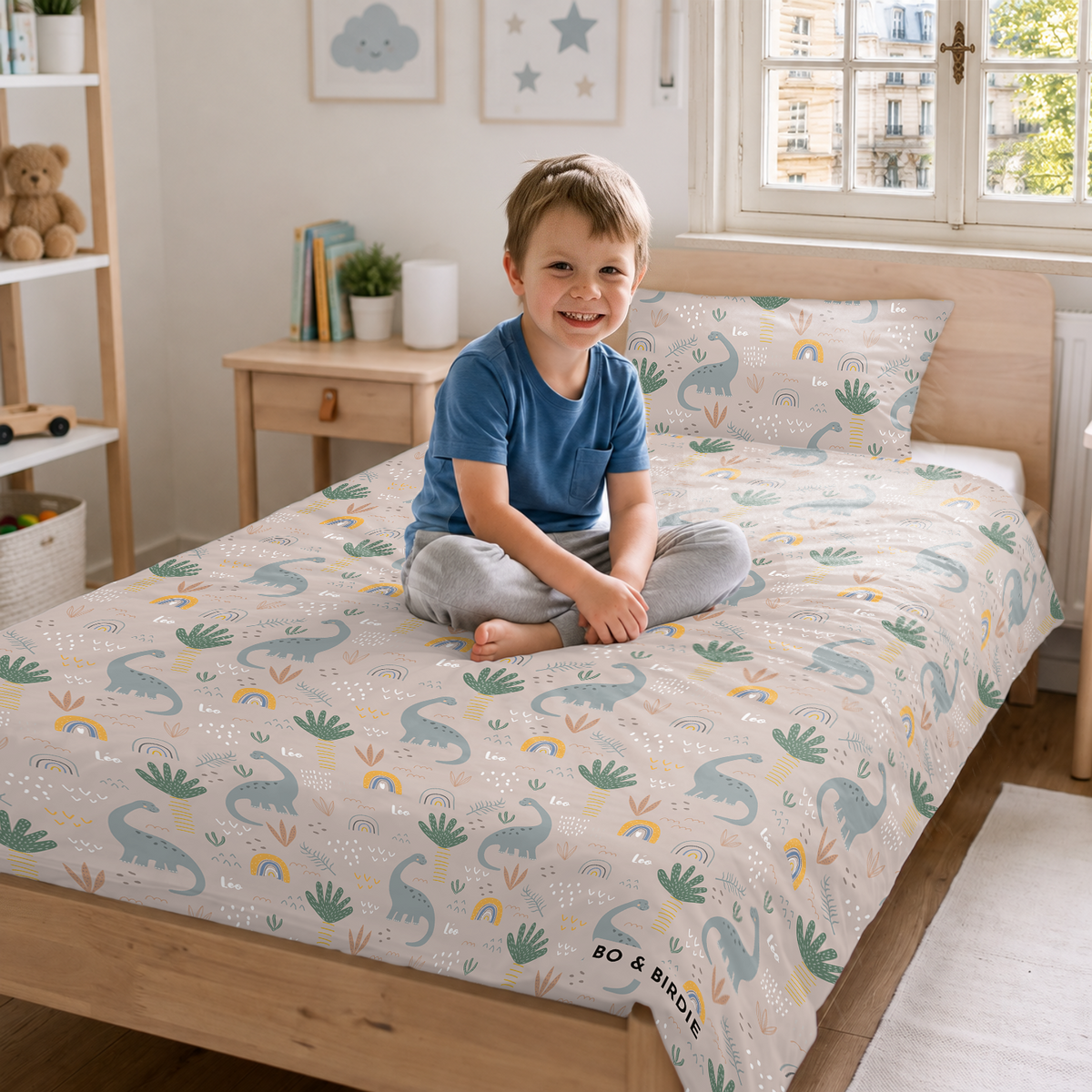 Petit garçon souriant assis sur un lit avec la parure Dinosaures market_france