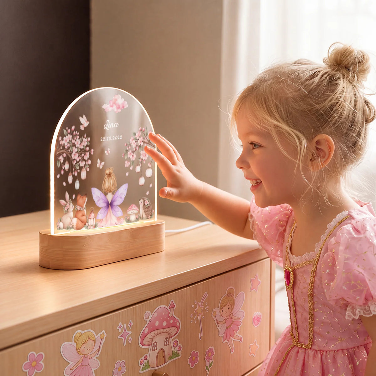 Fillette en robe de princesse touchant la veilleuse fée allumée sur la commode | market_france