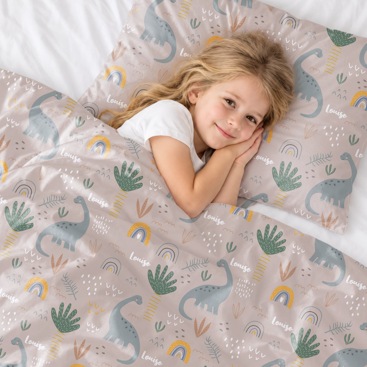 Petite fille blonde allongée sur l'oreiller de la parure de lit Dinosaures market_france