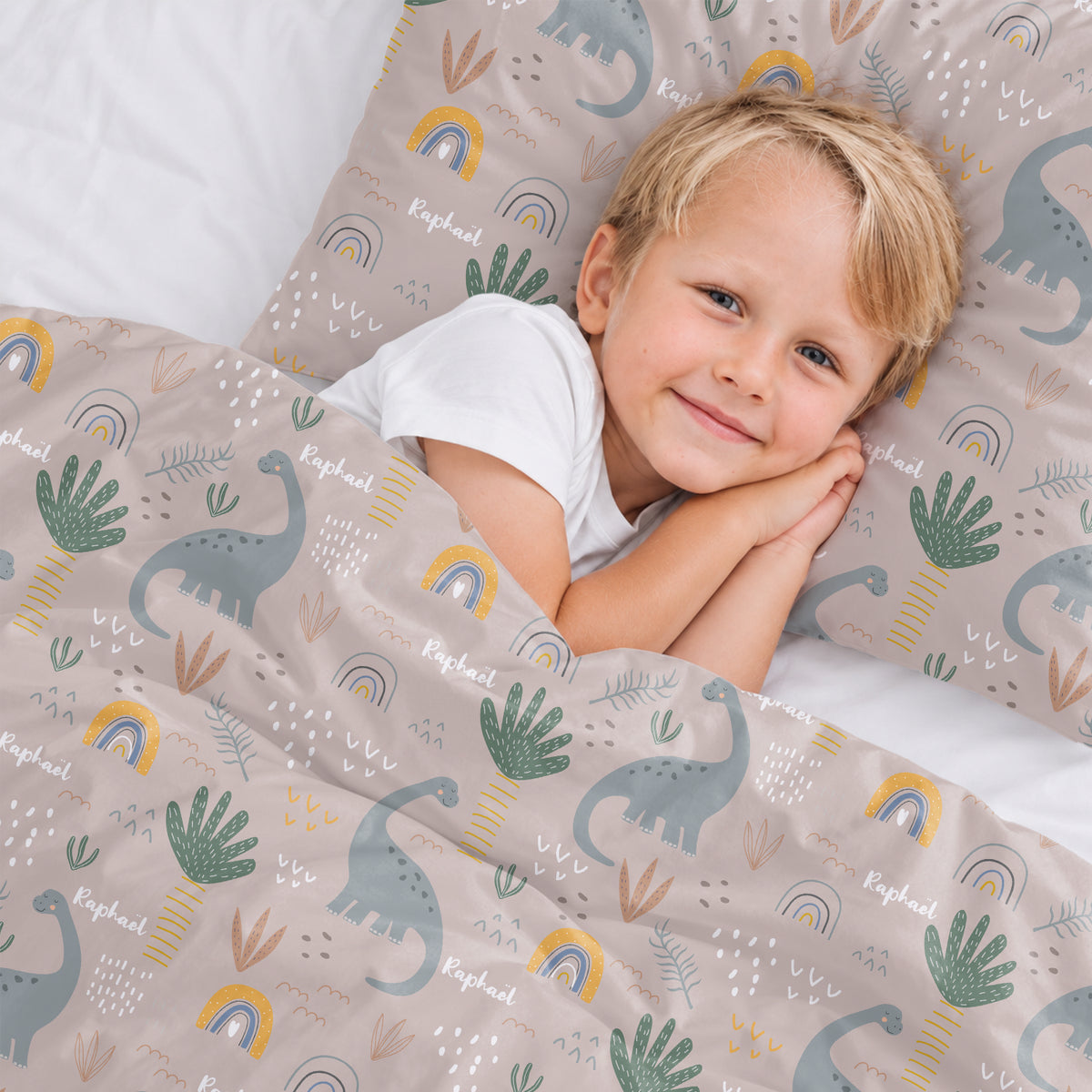 Petit garçon blond sourit dans la parure de lit Dinosaures avec prénom market_france